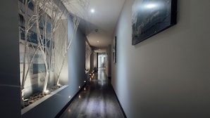 Un couloir doté d’un plancher en bois, d’un mur en verre où sont exposés des arbres, et d’un tableau encadré accroché au mur.