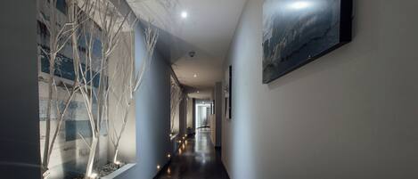 A hallway with a wooden floor, a glass wall with a tree display, and a framed picture on the wall.