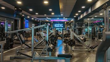 Un gimnasio con diversos equipos de ejercicio, un letrero de neón y un muro con espejos.