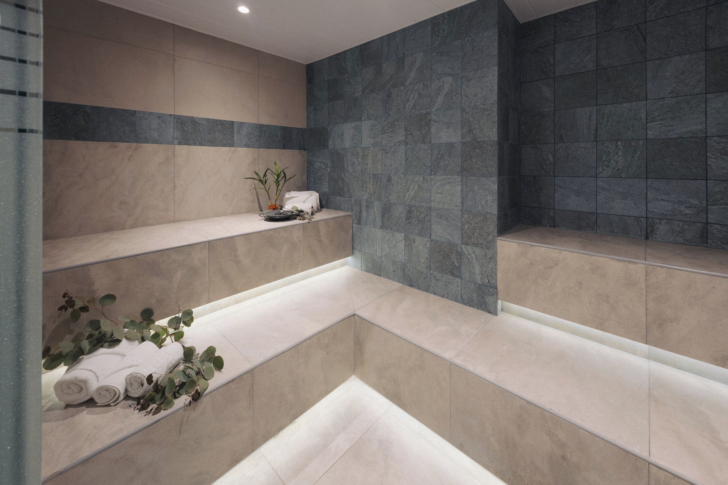 Een moderne badkamer met een ingebouwde bank, een klein plankje met een plant en een handdoekrek met handdoeken.