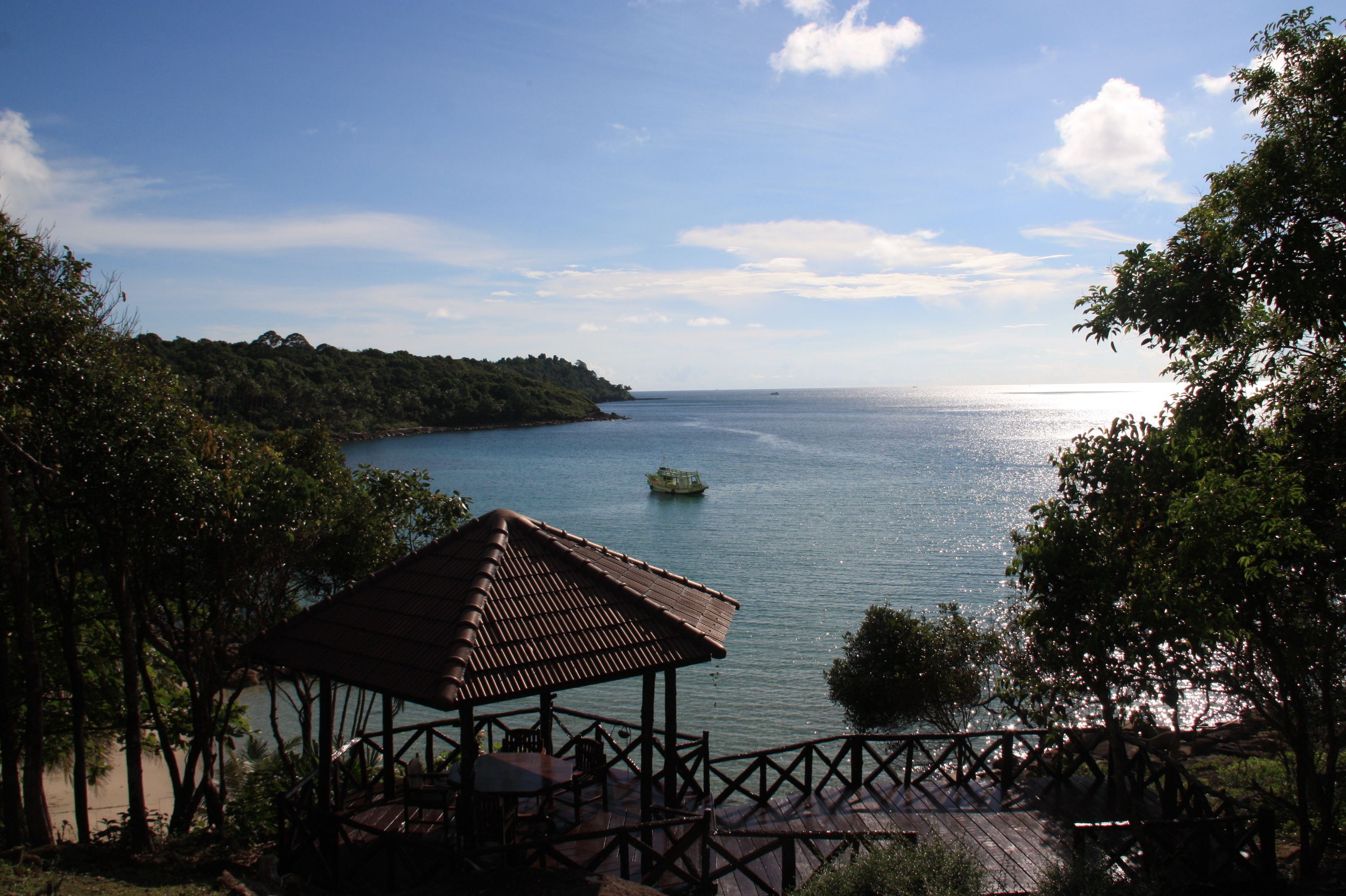 A wooden gazebo overlooking a calm body of water with a boat in the distance.
