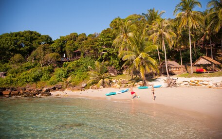 A beach with clear water, palm trees, and a hut.
