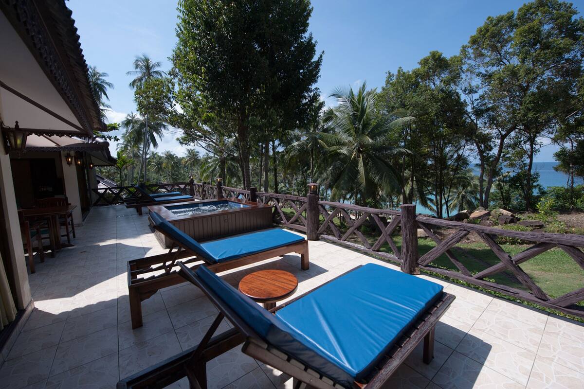 Un espace aménagé au bord de la piscine, avec des chaises longues et un jacuzzi, le tout entouré d’une clôture en bois et de palmiers.