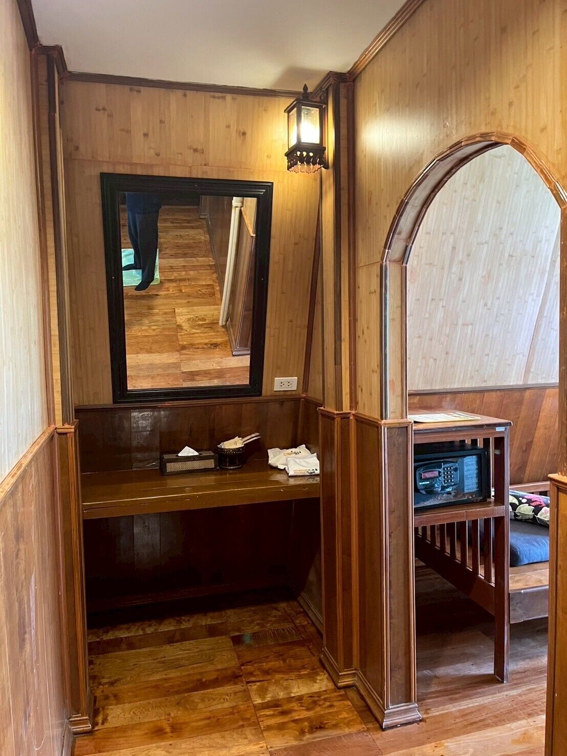 A wooden interior with a bench, a mirror, and a microwave shelf.