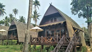 A thatched-roof bungalow with a wooden deck and staircase, surrounded by palm trees. - Koh Kood Beach Resort (Ko Kood)