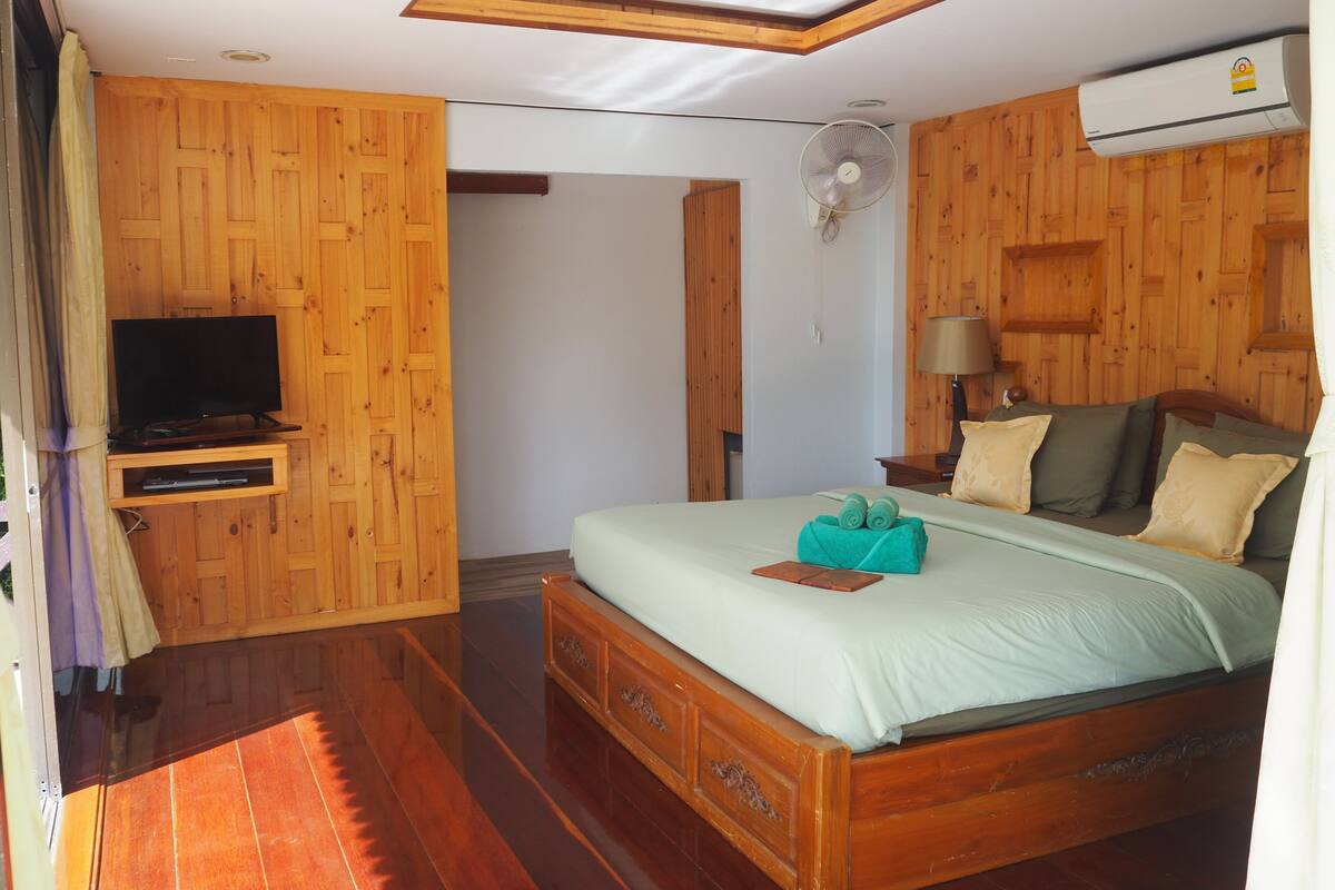 Une chambre à coucher aux murs lambrissés, comprenant un lit, un téléviseur, un ventilateur et une lampe.