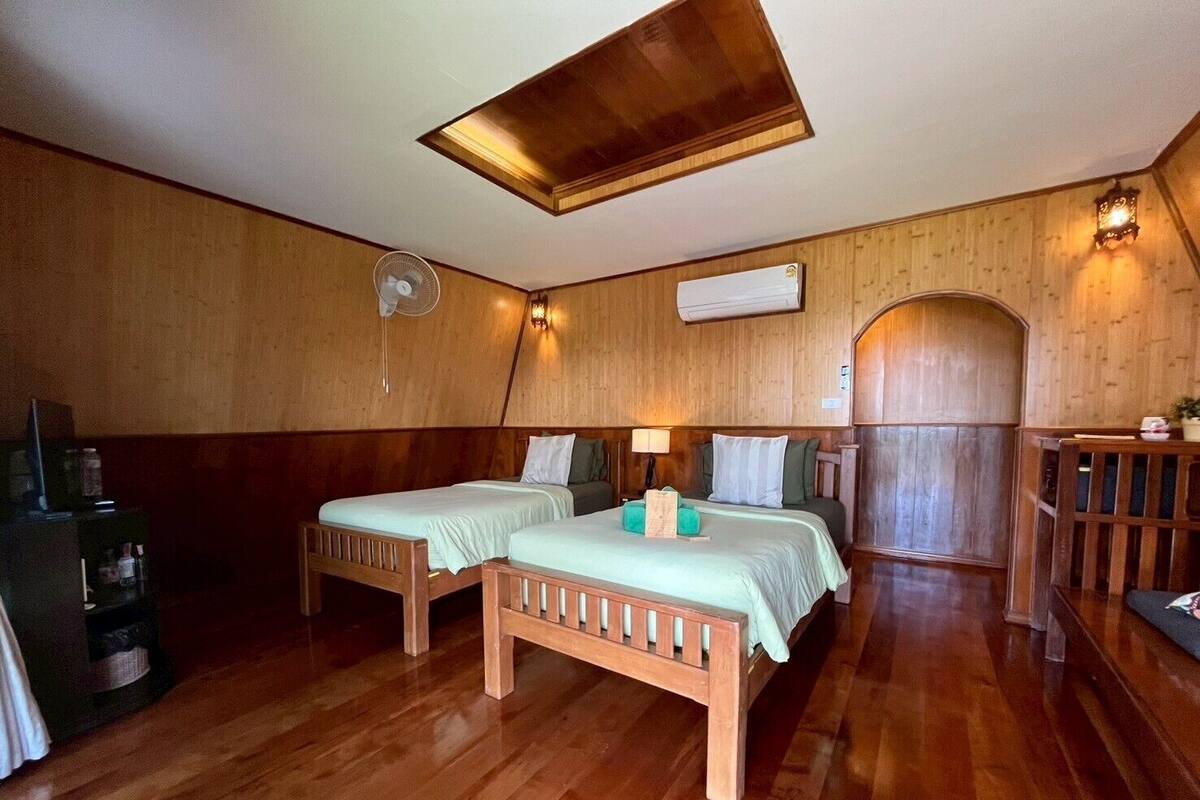 Une pièce avec deux lits en bois, un ventilateur de plafond, un radiateur fixé au mur et un banc en bois.