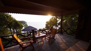A covered outdoor seating area with a table and chairs, overlooking a body of water and greenery. - Koh Kood Beach Resort (Ko Kood)