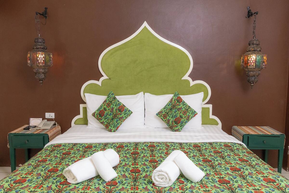 A hotel room with a bed, green nightstands, and decorative wall sconces.