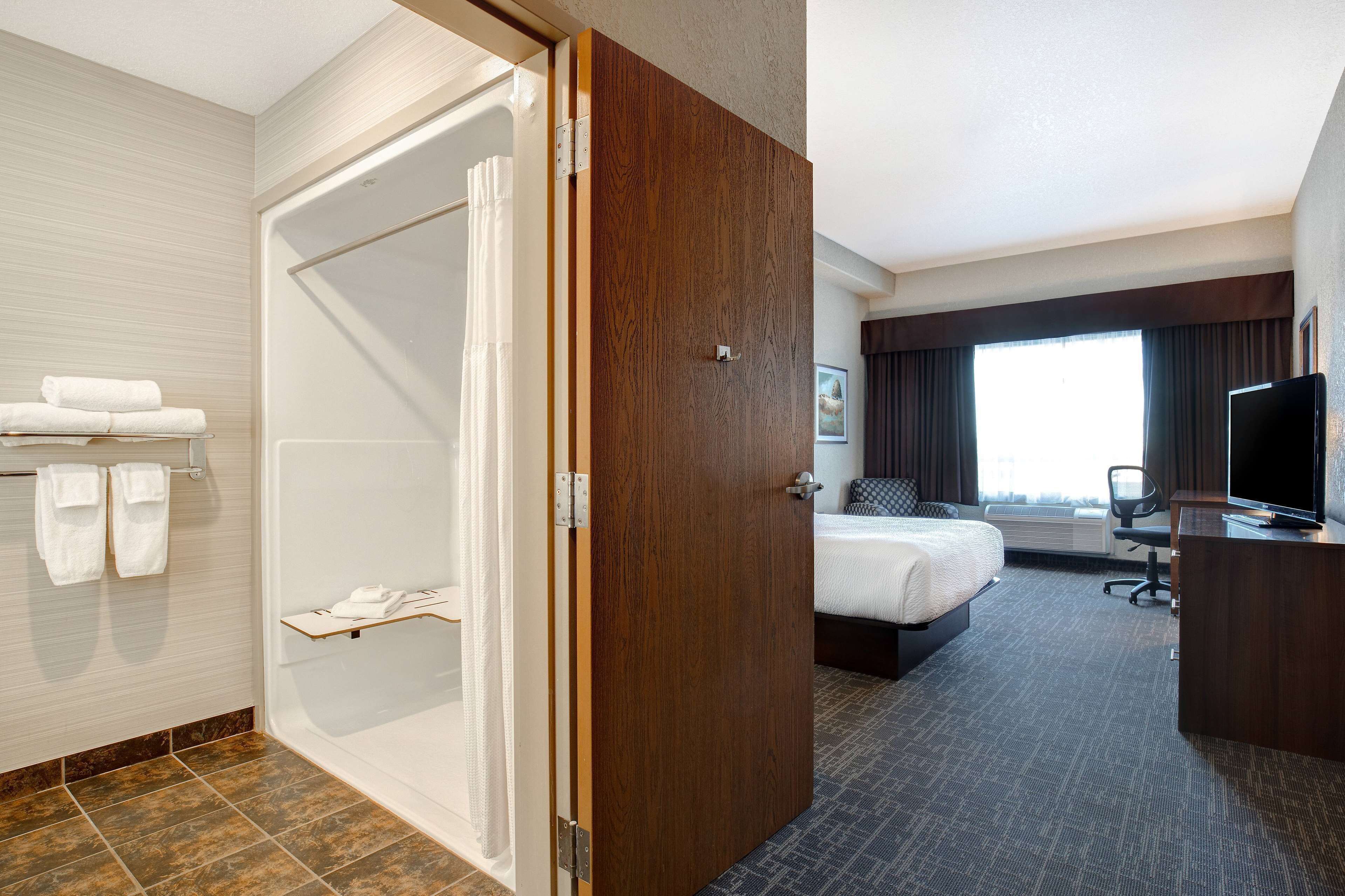 A hotel room with a shower, a bed, a desk, and a TV.