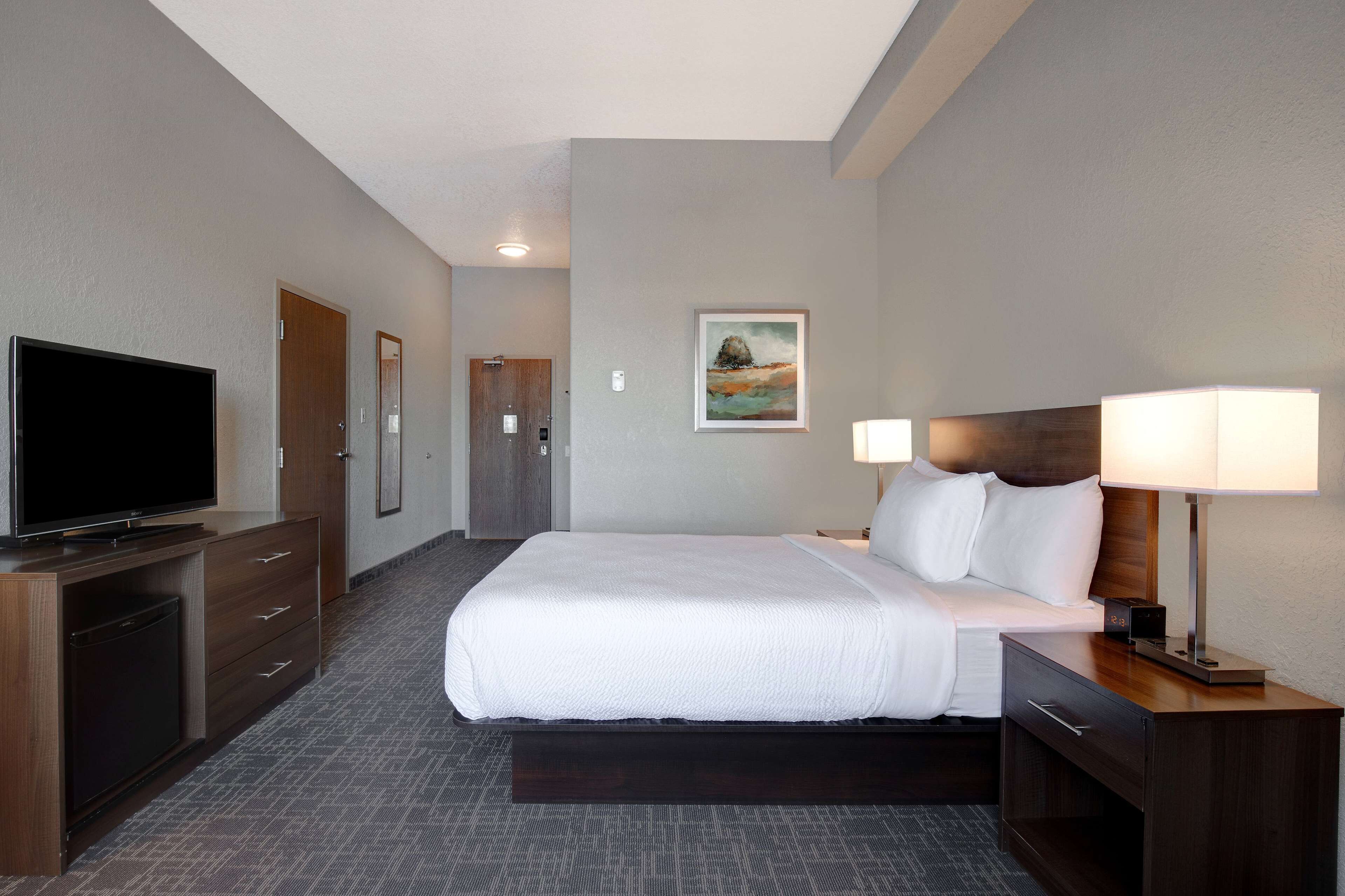 A hotel room with a large bed, a TV, a desk with a lamp, and a painting on the wall.