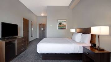 A hotel room with a large bed, a TV, a desk with a lamp, and a painting on the wall.