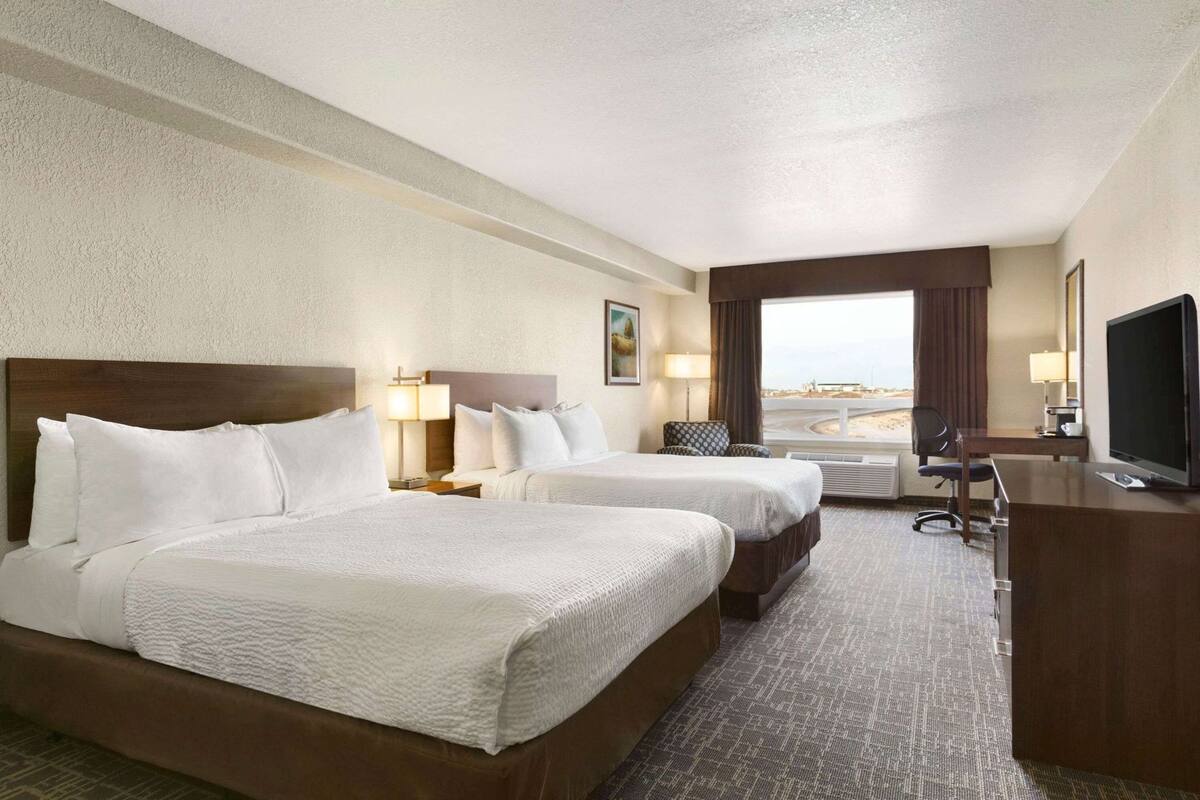 A hotel room with two beds, a desk, a television, and a view of the beach.