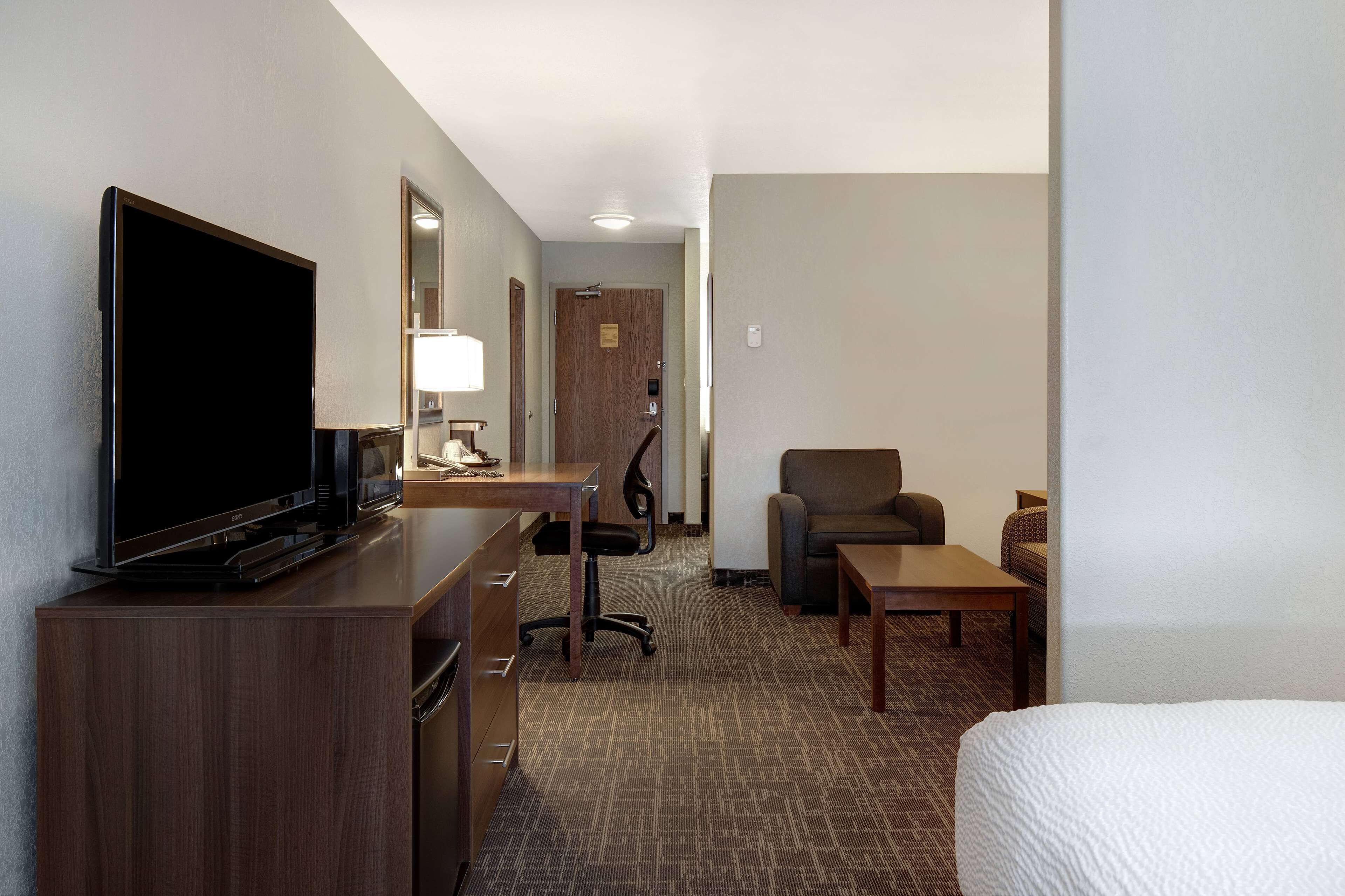 A hotel room with a flat-screen TV, a desk with a lamp, a chair, a sofa, and a bed.