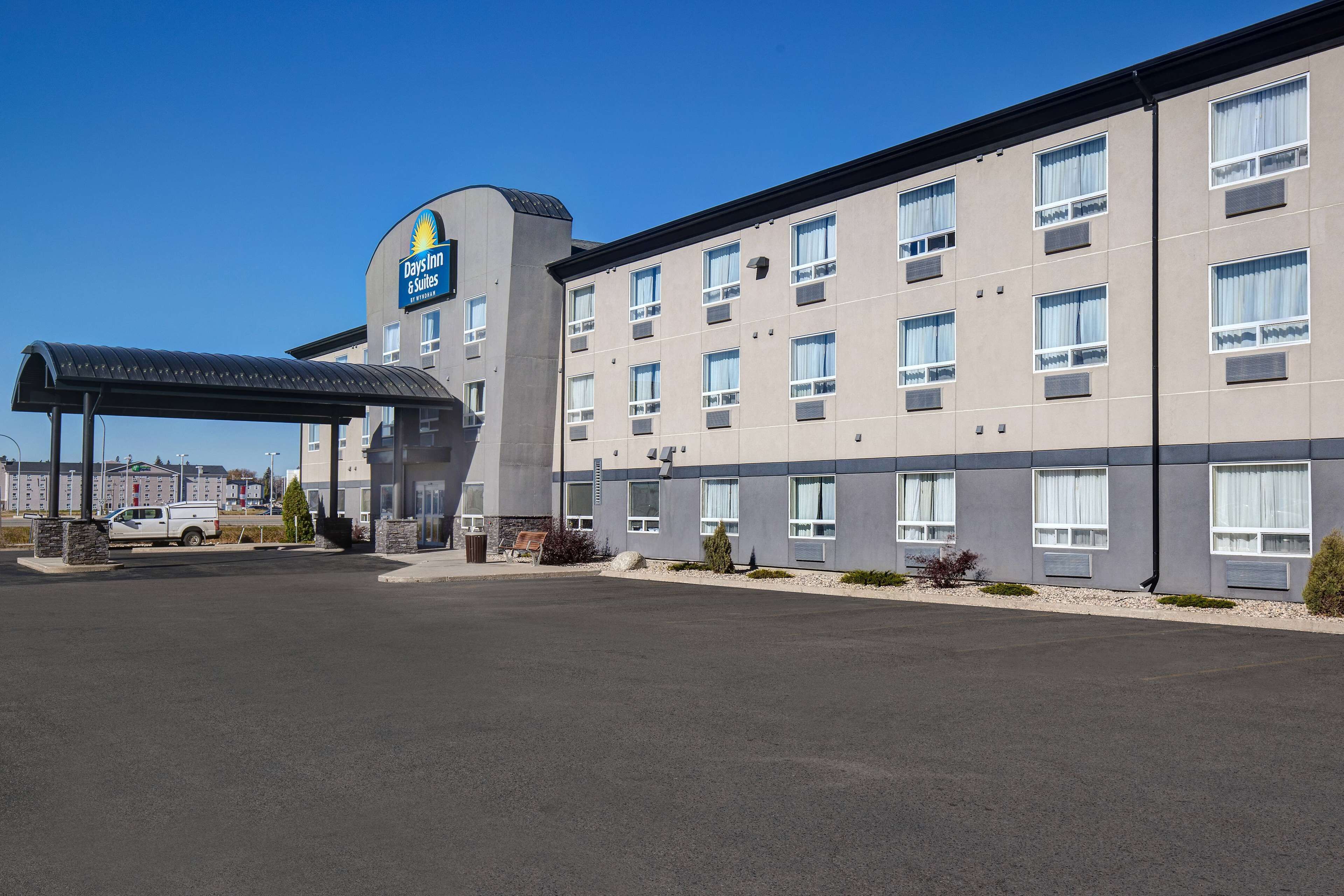Edificio de Days Inn & Suites con una zona de estacionamiento techada y una camioneta blanca estacionada afuera.
