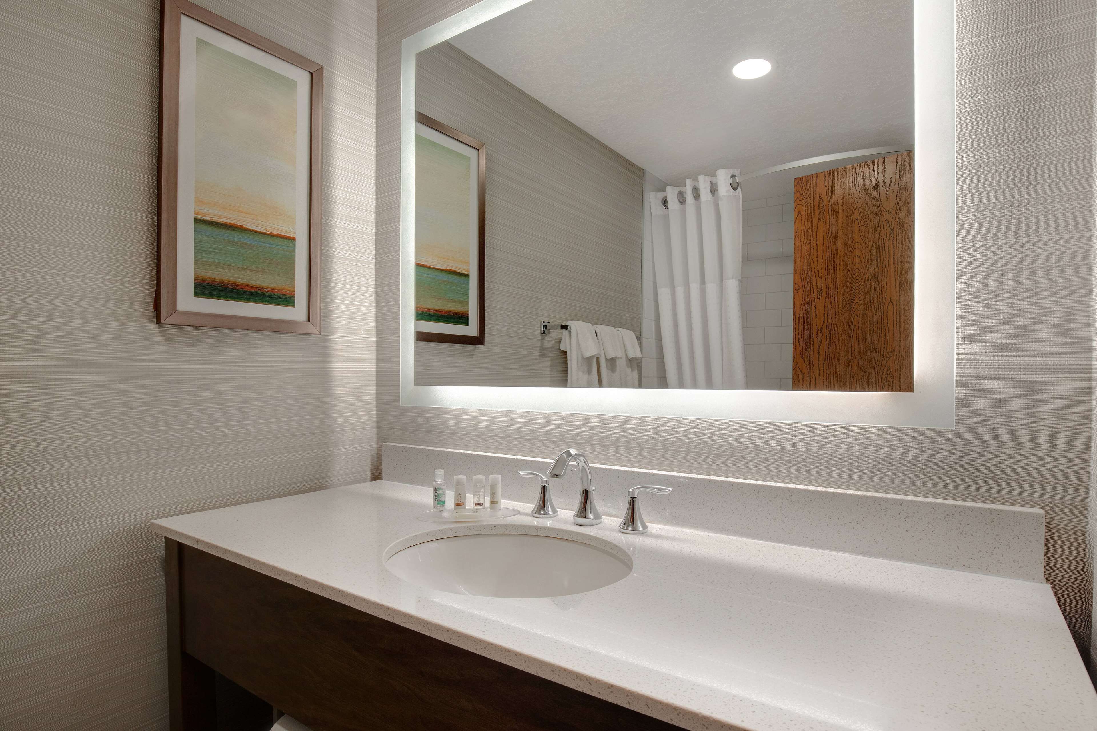 A modern bathroom with a white sink, two faucets, and a large mirror.