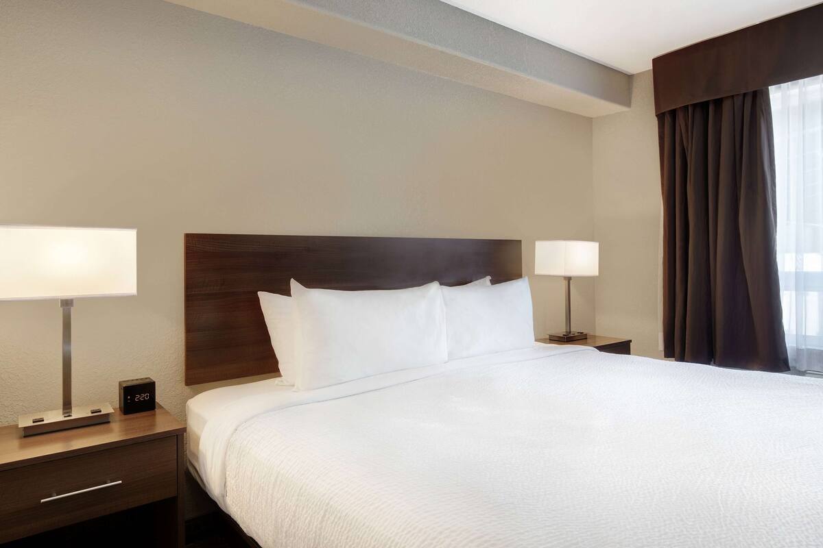 A hotel room with a large bed, two bedside tables, a nightstand, a digital clock, and a window with curtains.