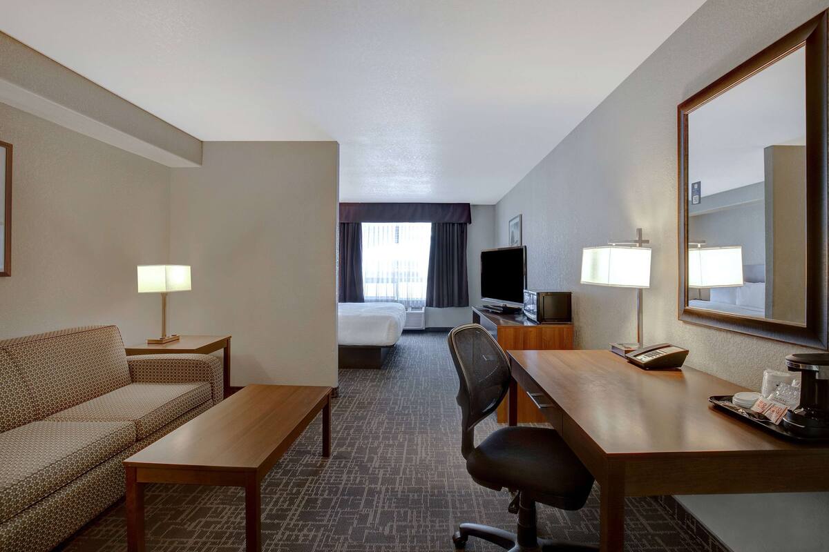 A hotel room with a sofa, a desk, a chair, a bed, a TV, and a large mirror.