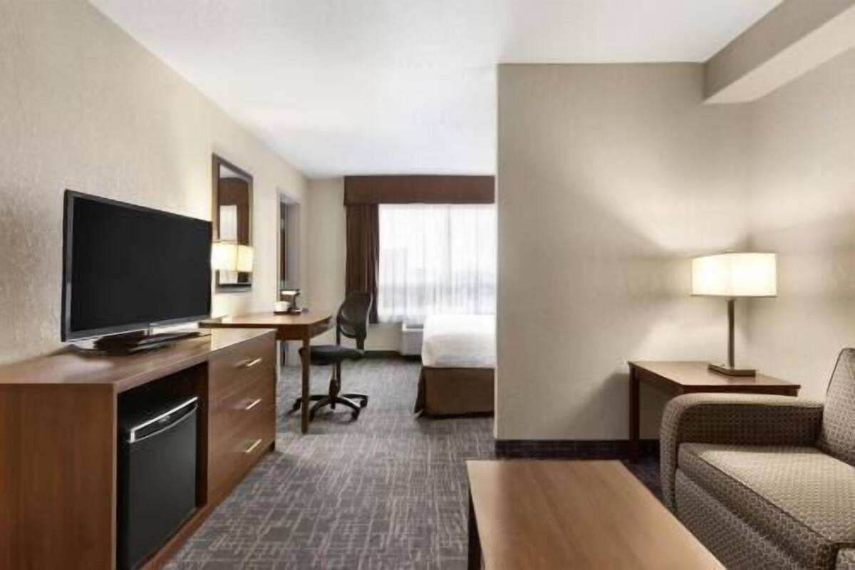 A hotel room with a TV, desk, chair, bed, and a sofa.