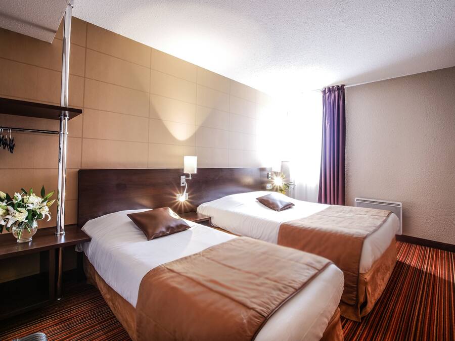 A hotel room with two beds, a nightstand, a lamp, and a vase of flowers.