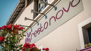 A building with a sign that reads "Vrestonovo" and a window with a view of red flowers.