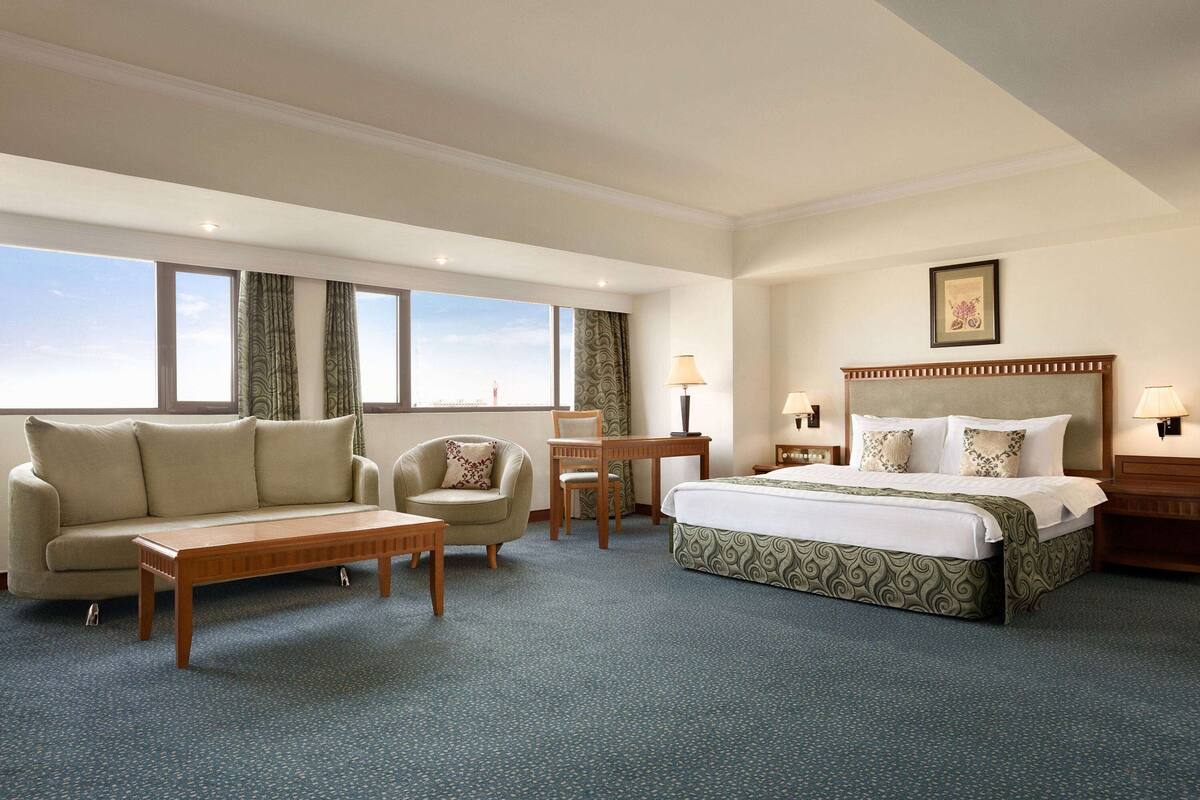 A hotel room with a large bed, a sofa, a small table, and a chair.