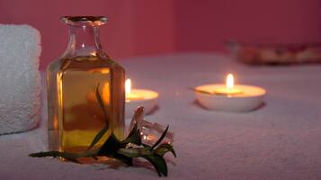 A bottle of liquid, a lit candle, and a white towel on a surface.