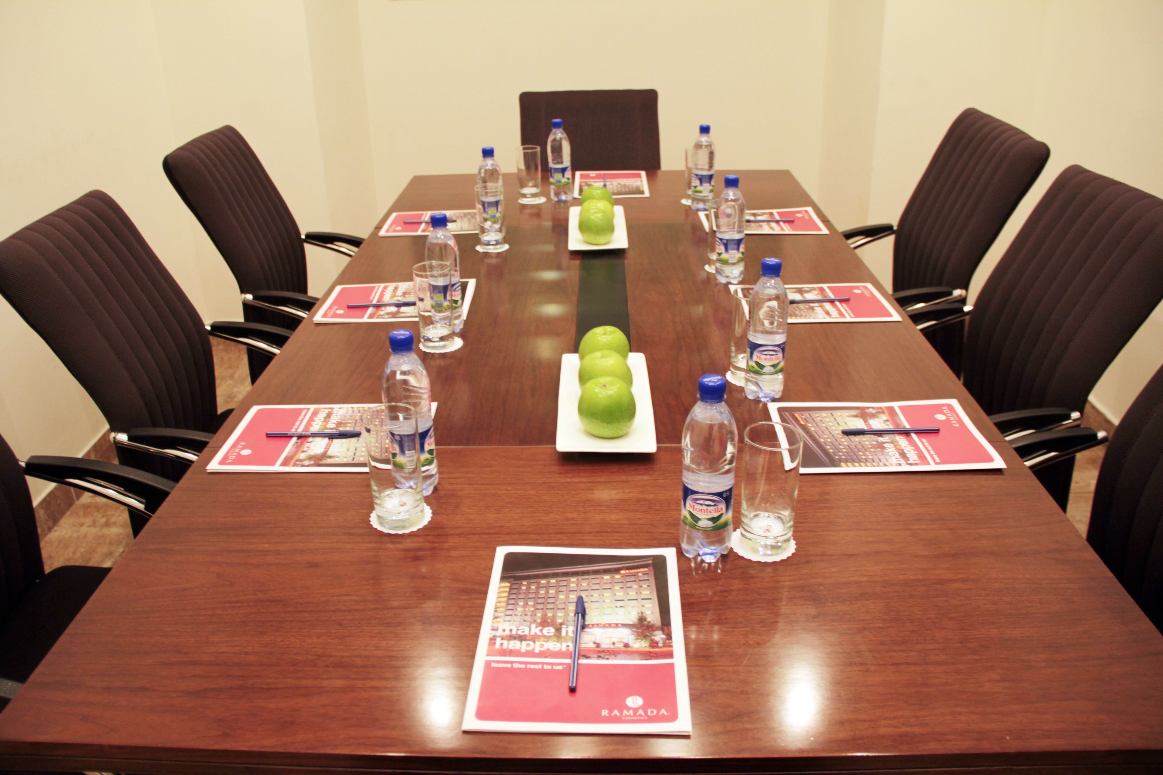 A conference room with a long table, chairs, water bottles, and a plate of green apples.