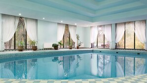 A large indoor swimming pool with clear blue water, surrounded by a checkered floor, large windows with white curtains, and potted plants. - Ramada by Wyndham Tashkent (Tashkent)