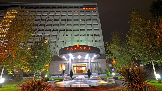 A hotel with a prominent "RAMADA" sign, a well-lit entrance, and a landscaped garden with a fountain. - Ramada by Wyndham Tashkent (Tashkent)