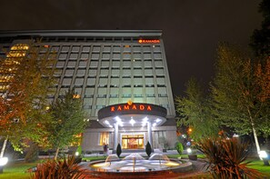 A hotel with a prominent "RAMADA" sign, a well-lit entrance, and a landscaped garden with a fountain. - Ramada by Wyndham Tashkent (Tashkent)