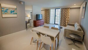 Un salon moderne comprenant un coin repas, un canapé, un téléviseur et une grande fenêtre avec des rideaux.