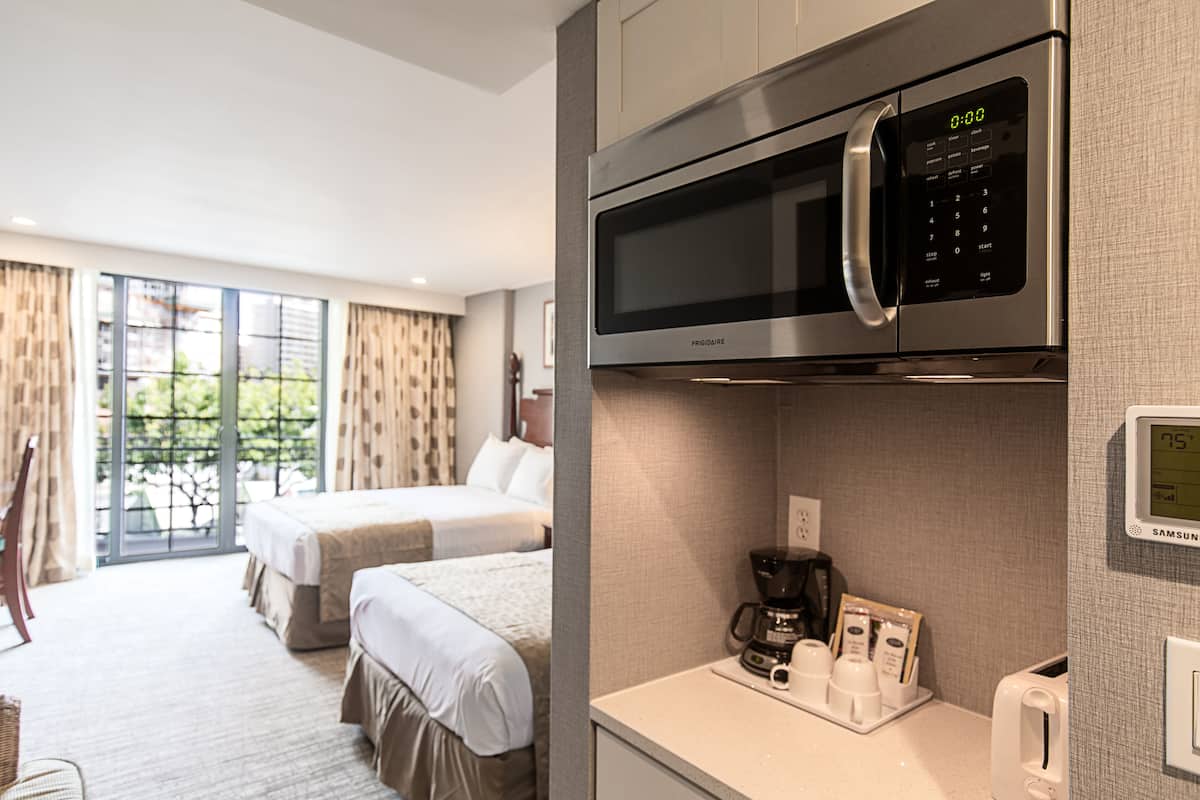 A hotel room with a kitchenette, including a microwave, coffee maker, and toaster. There are two beds and a large window with curtains.