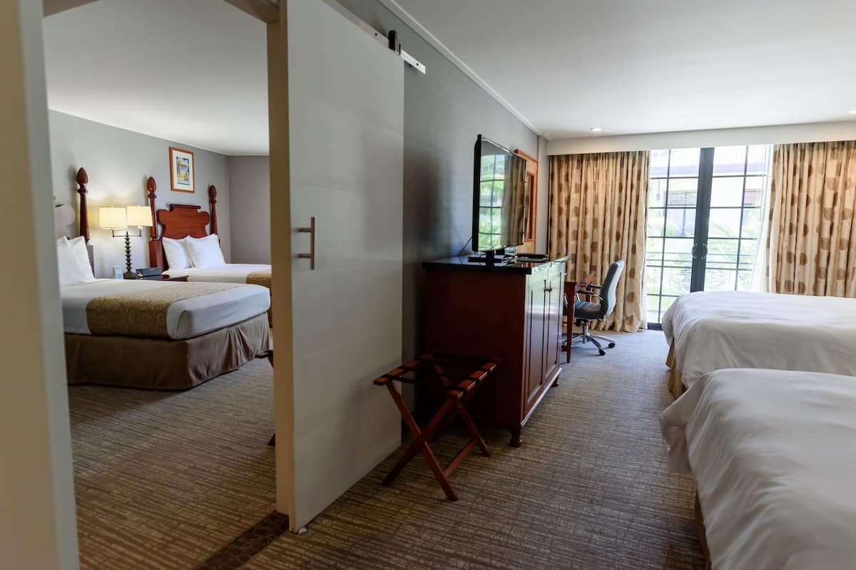 A hotel room with two beds, a desk with a chair, a large mirror, and a window with curtains.