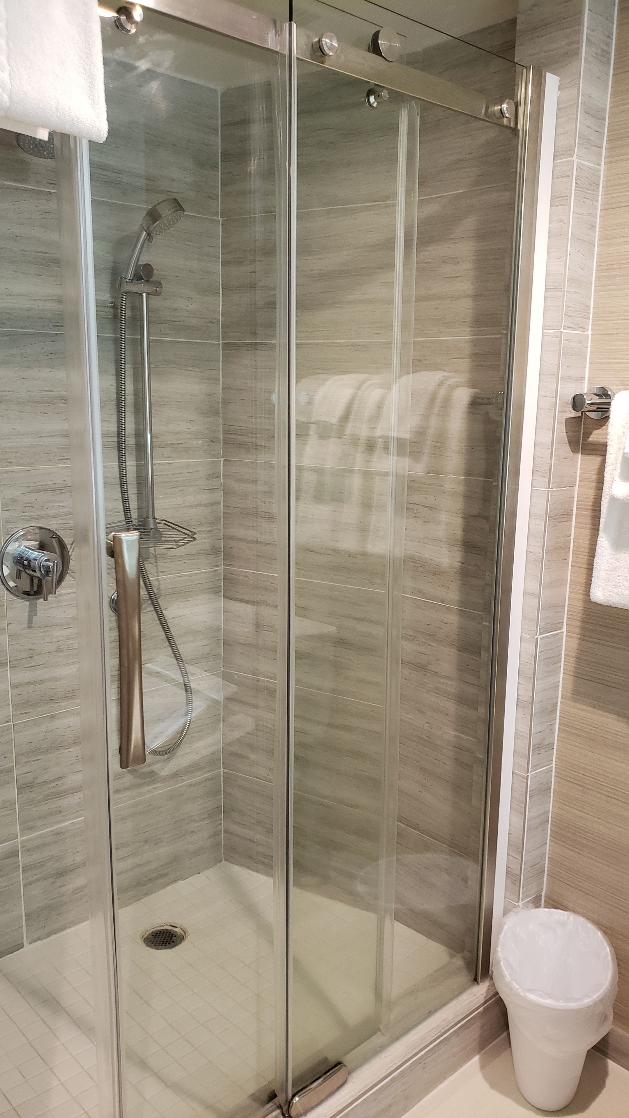 A glass-enclosed shower with a handheld showerhead and a wall-mounted control panel.