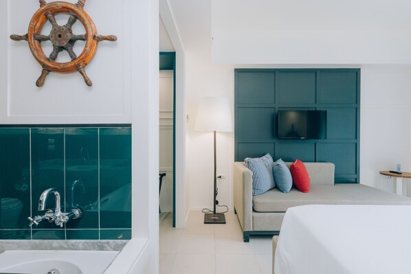 Habitación de hotel con baño, sofá con almohadones, televisor montado en la pared y una lámpara.