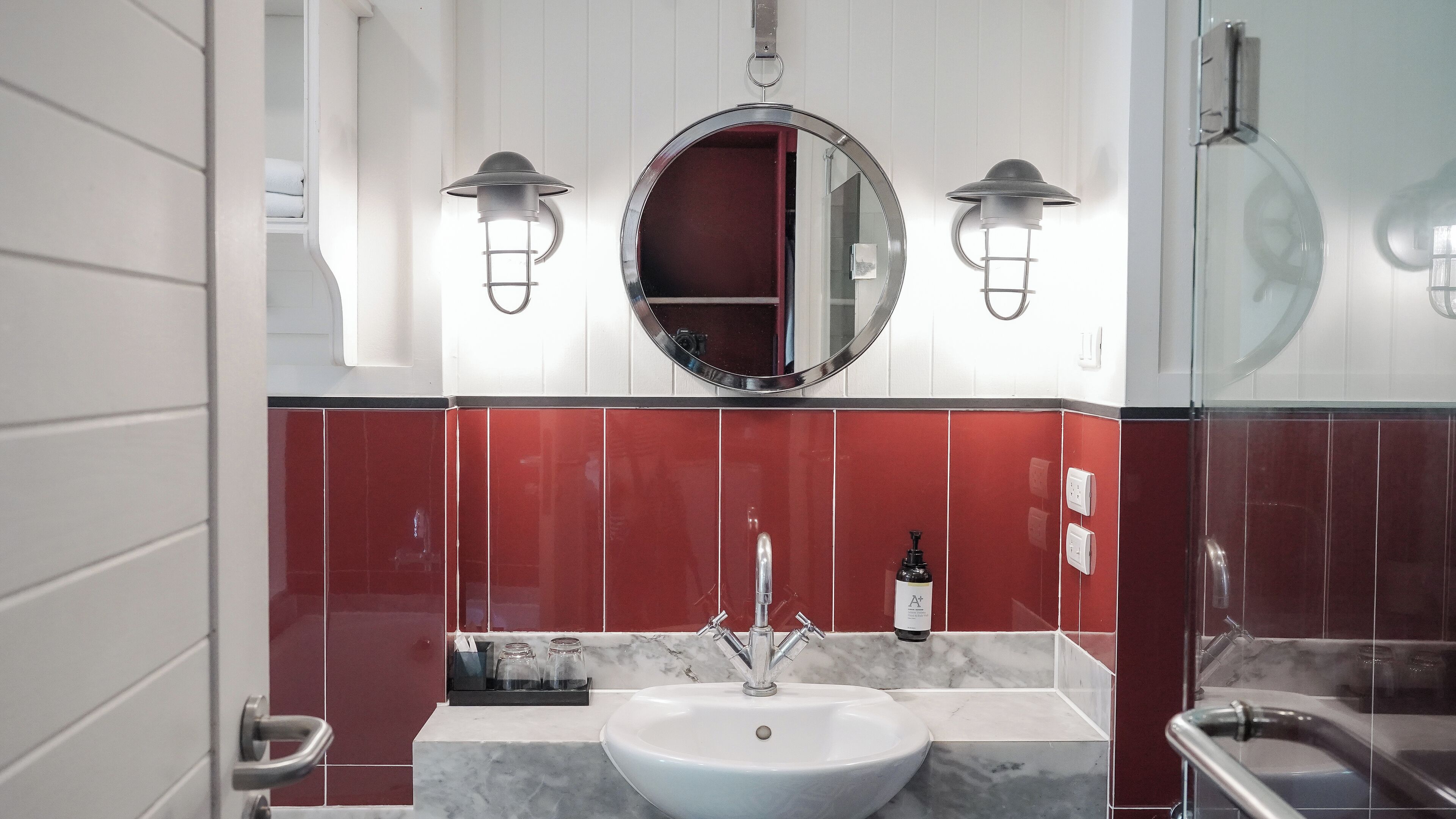 Ein Badezimmer mit einem weißen Waschbecken, roten Fliesenwänden und zwei Wandleuchten.