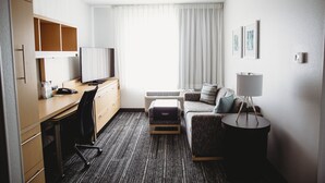 A hotel room with a desk, chair, sofa, and a small side table with a lamp. - TownePlace Suites by Marriott Aberdeen (Aberdeen)
