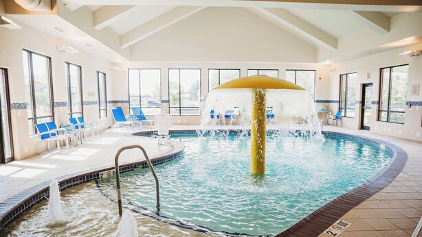 An indoor swimming pool with a central water feature, surrounded by lounge chairs and large windows. - TownePlace Suites by Marriott Aberdeen (Aberdeen)