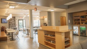 A modern cafe with a breakfast bar, seating area, and a refrigerator stocked with beverages. - TownePlace Suites by Marriott Aberdeen (Aberdeen)