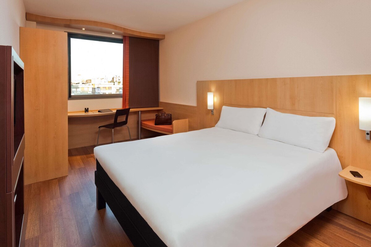 Una habitación de hotel con una cama grande, un escritorio, una silla y un ventanal con vistas.