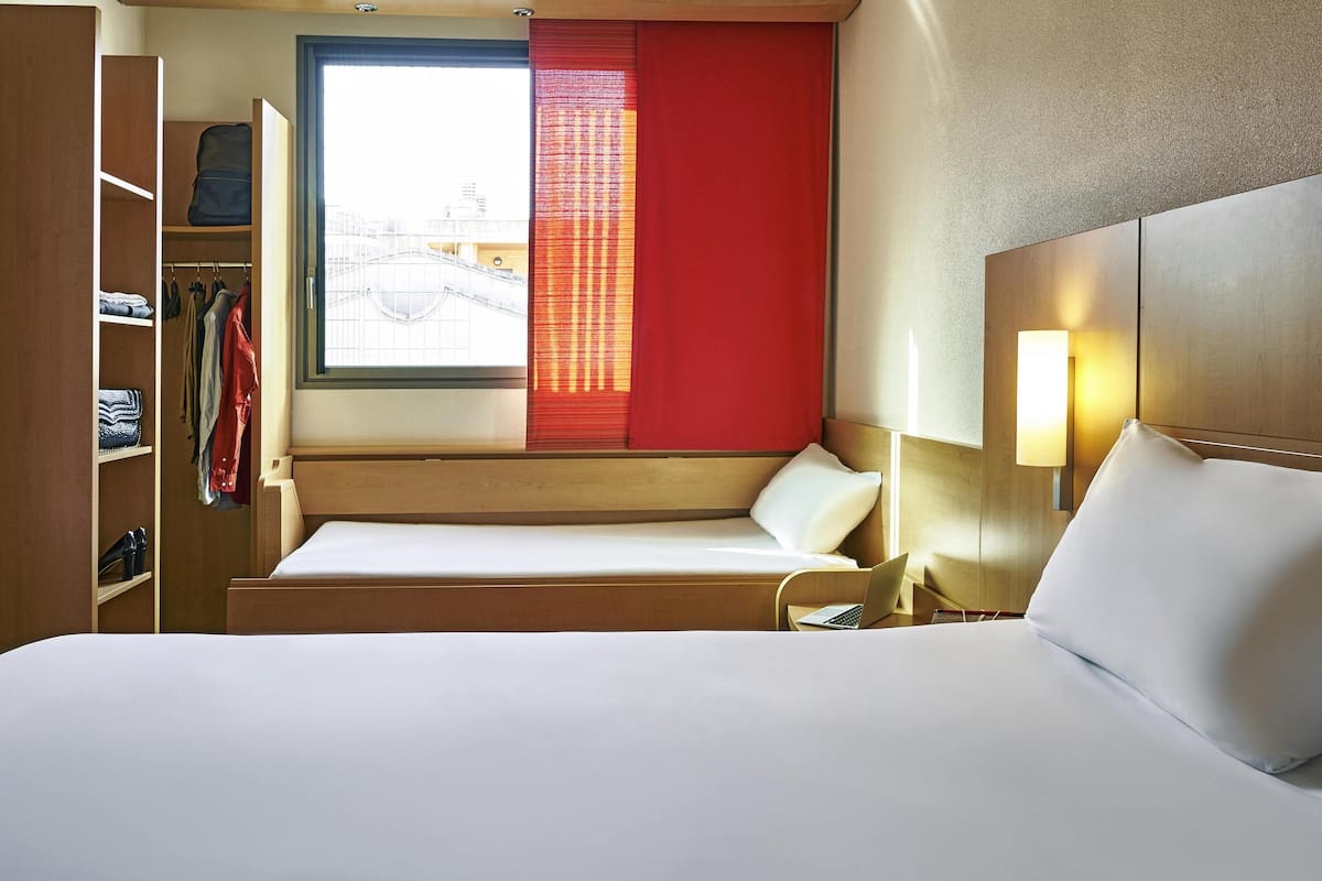 Habitación de hotel con cama, escritorio, ordenador portátil, ventana con cortina roja y armario.