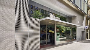 Un hôtel moderne doté d’une façade en verre, d’une entrée bien visible et d’un panneau indiquant l’emplacement du parking.