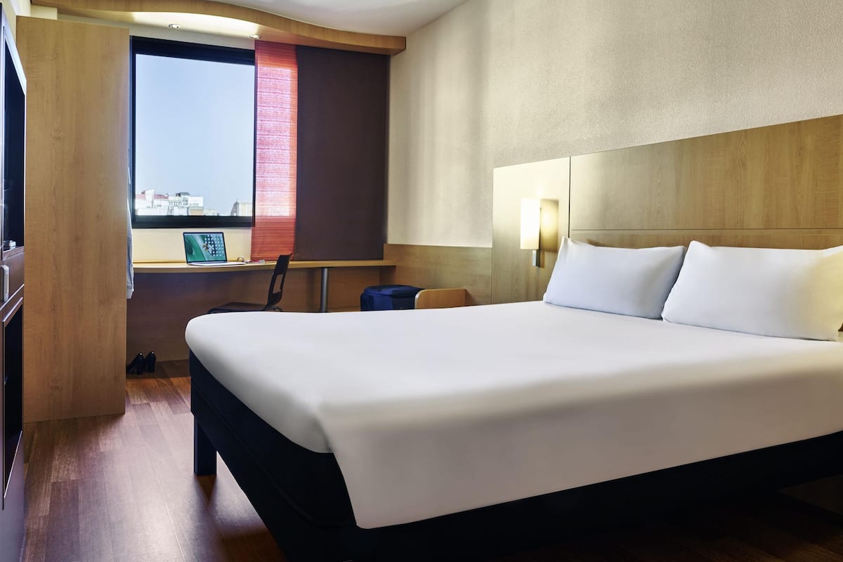 Una habitación de hotel con una cama grande, un escritorio con una computadora portátil, una silla y una ventana con vistas.