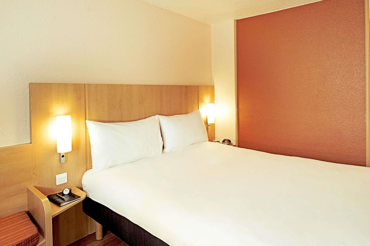 Una habitación de hotel con una cama grande, cabecero de madera, lámparas de noche y una mesita de noche.