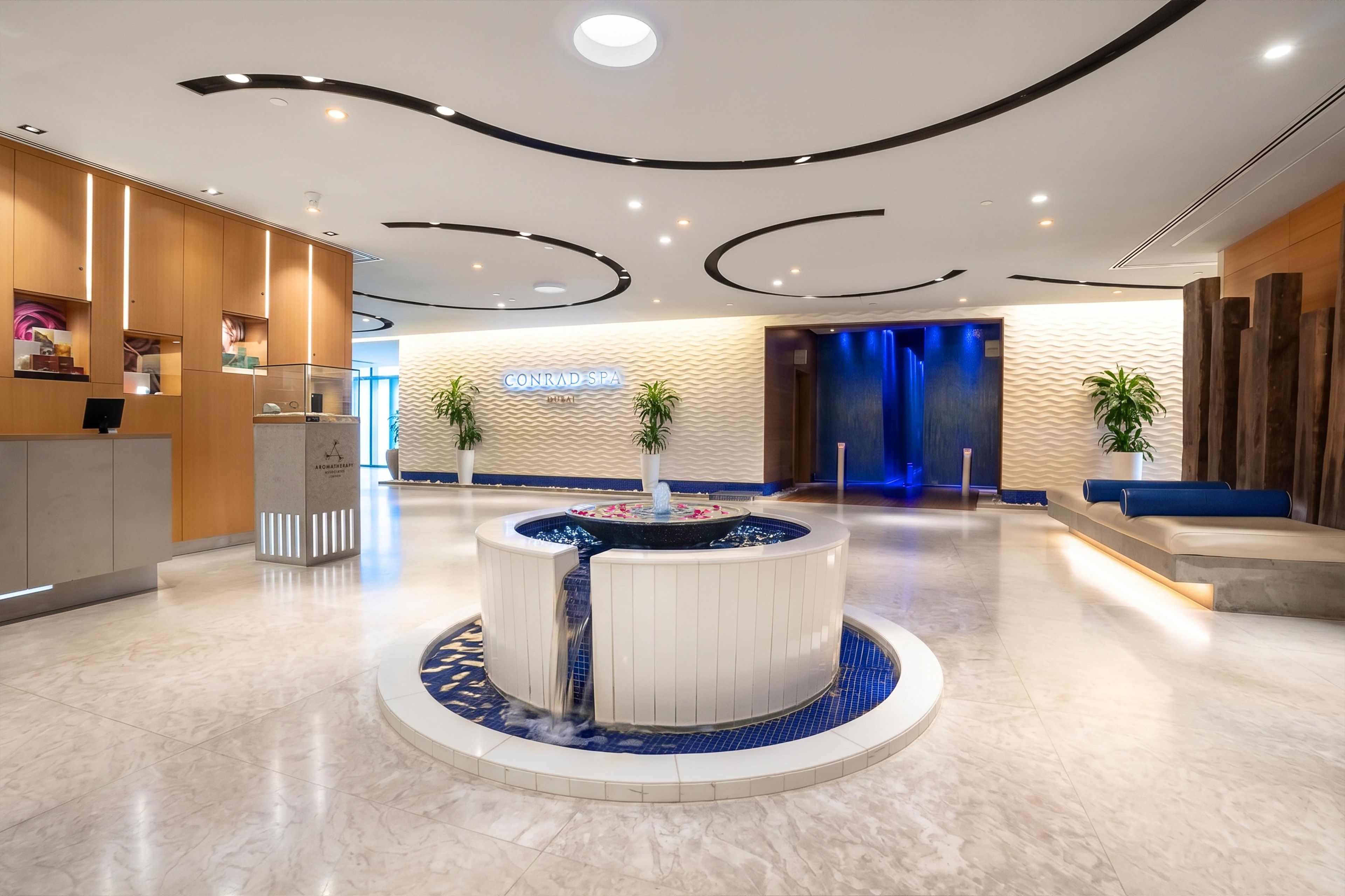 En moderne lobby med et centralt vandelement, en receptionsdisk og et skilt til spa-afdelingen.