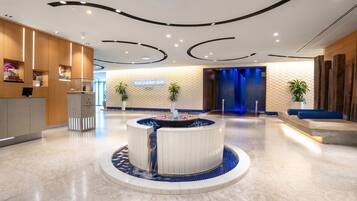 En moderne lobby med et centralt vandelement, en receptionsdisk og et skilt til spa-afdelingen.