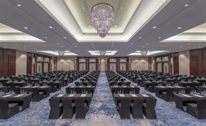 A large conference room with rows of tables and chairs, a chandelier, and a patterned carpet.