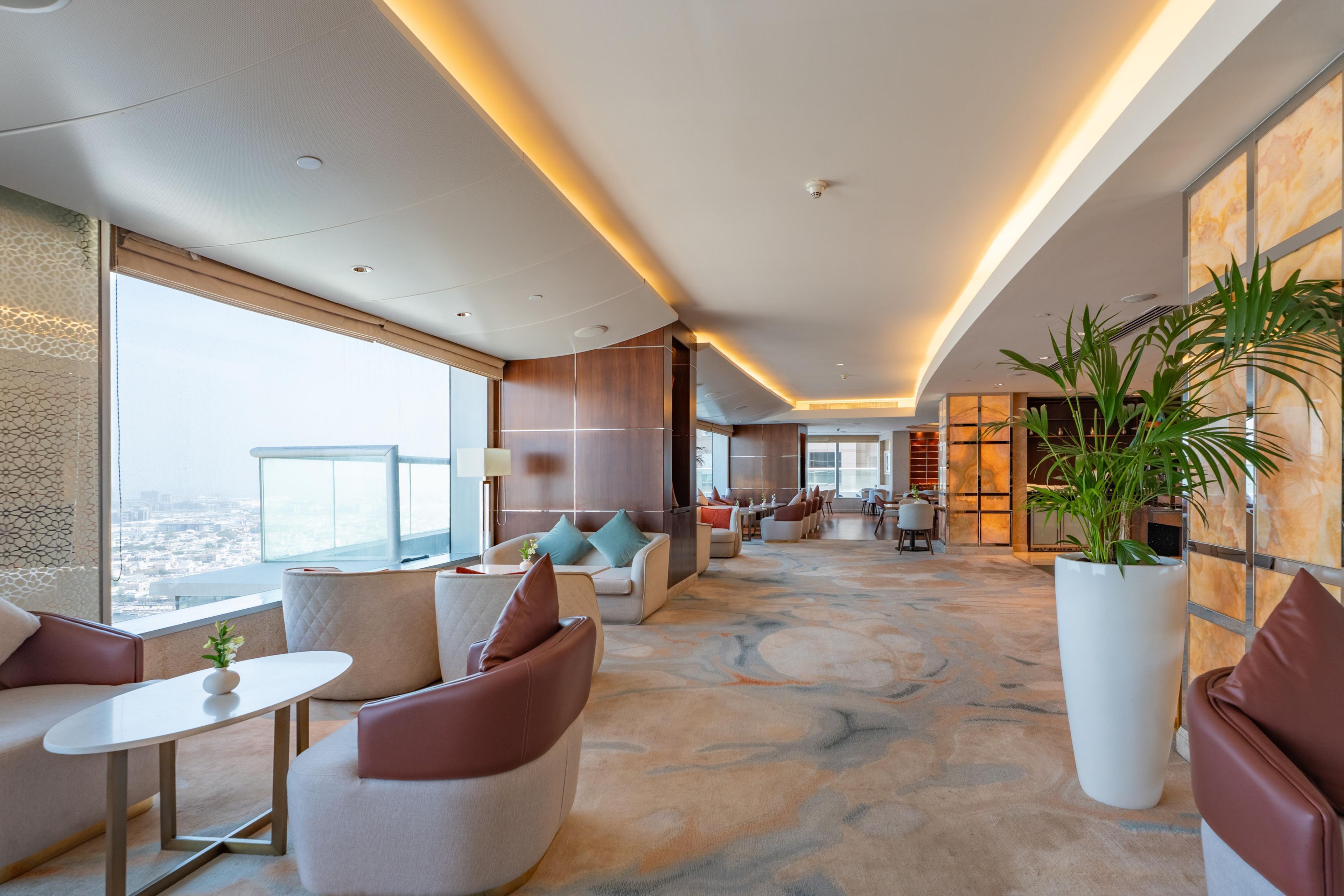 A modern hotel lobby with seating areas, a large window offering a city view, and a reception desk.