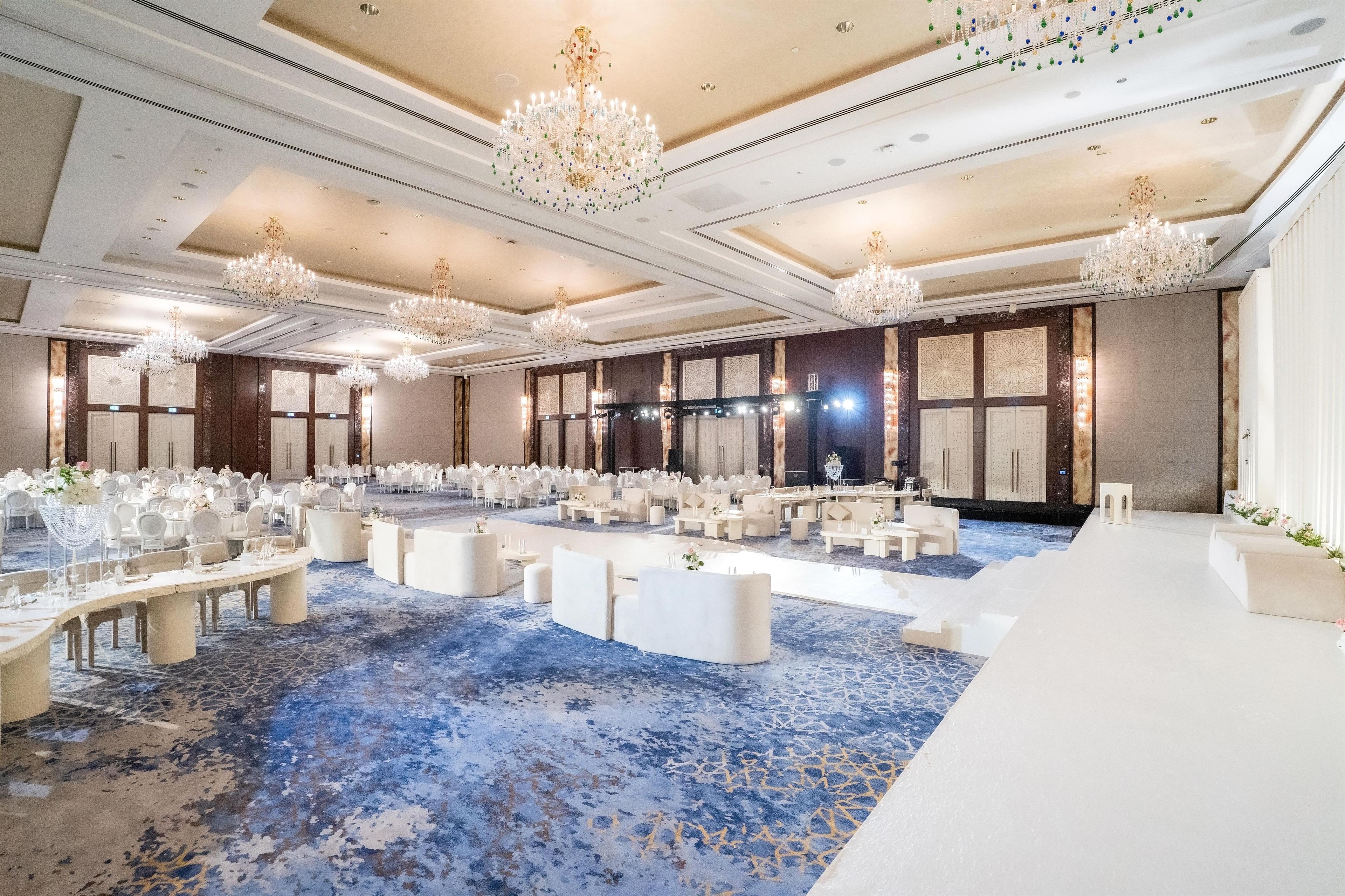 A large banquet hall with round tables, white chairs, and a blue patterned carpet.